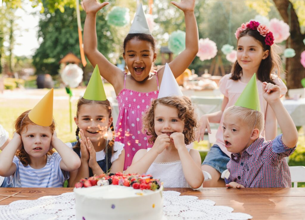 Down syndrome child with friends on birthday party outdoors in garden